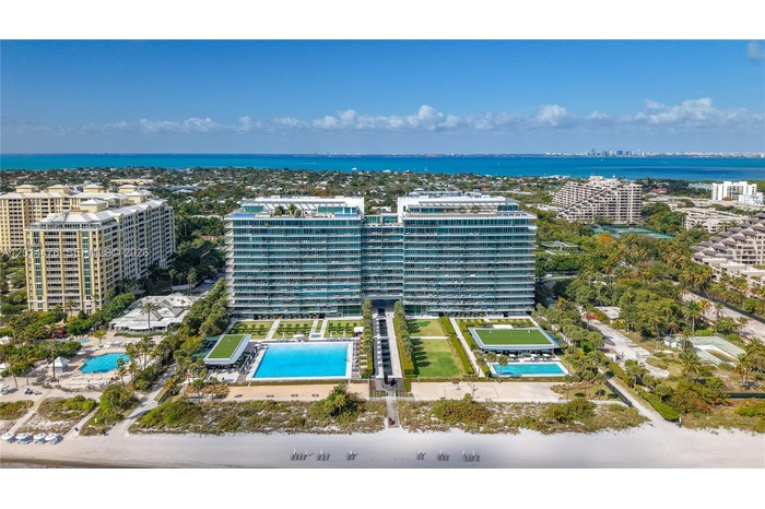 Full Exterior / Beachfront Overview – A broad exterior view presents the full building, landscaped grounds, resort-style pools, and direct beachfront 