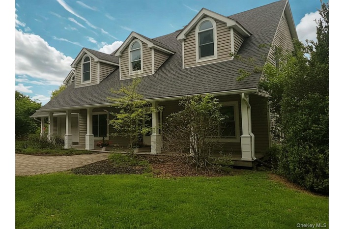 Dormered residence featuring a covered front porch with white columns, horizontal siding, and a shingle roof