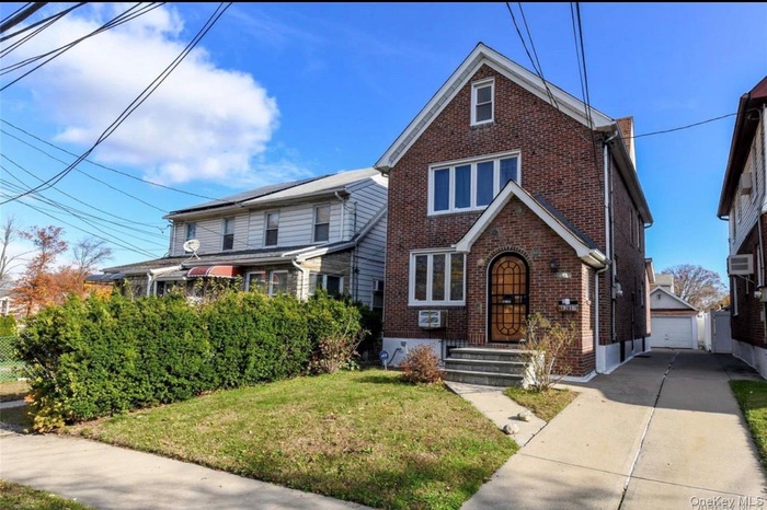 Brick residence featuring a gabled roofline, arched entry door, multiple window configurations, concrete driveway, and a detached garage