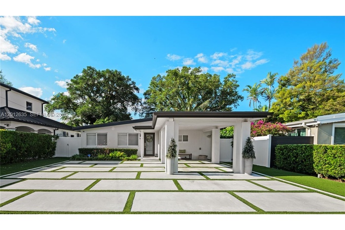 Fully concrete front yard with large-format pavers, artificial turf grid, and privacy landscaping — one-car covered carport with white concrete column
