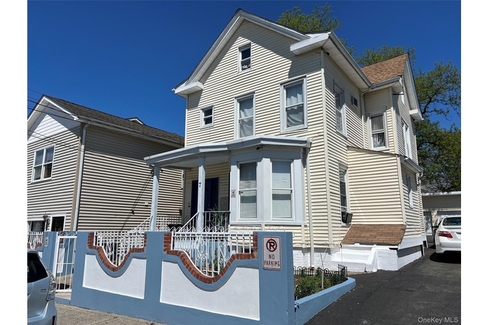 Cream-colored siding exterior featuring a covered porch with white railings, a bay window, and a gabled roofline