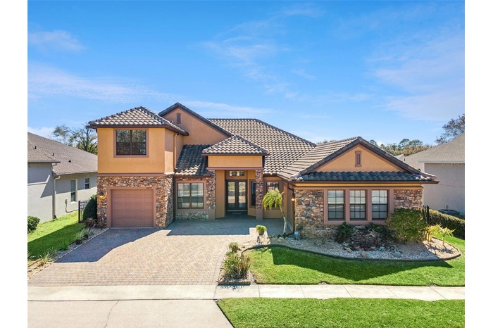 Elegant Sanford, FL home with striking stone façade, barrel tile roof, and an expansive paver driveway that enhances its upscale curb appeal.