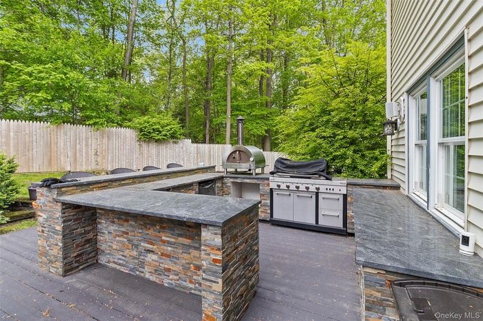 Outdoor kitchen featuring a U-shaped bar with stacked stone facade and dark countertops, a built-in grill, and an additional outdoor cooking appliance