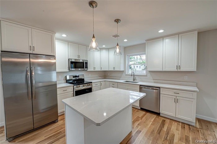 Kitchen featuring a central island with a white quartz counters/ countertop, white shaker-style cabinetry, stainless steel appliances, pendant lightin