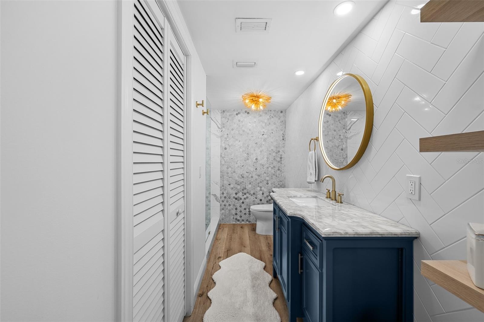 Renovated bath with herringbone white subway tile, a custom navy vanity, white marble counter, brass fixtures, and a walk-in marble shower.