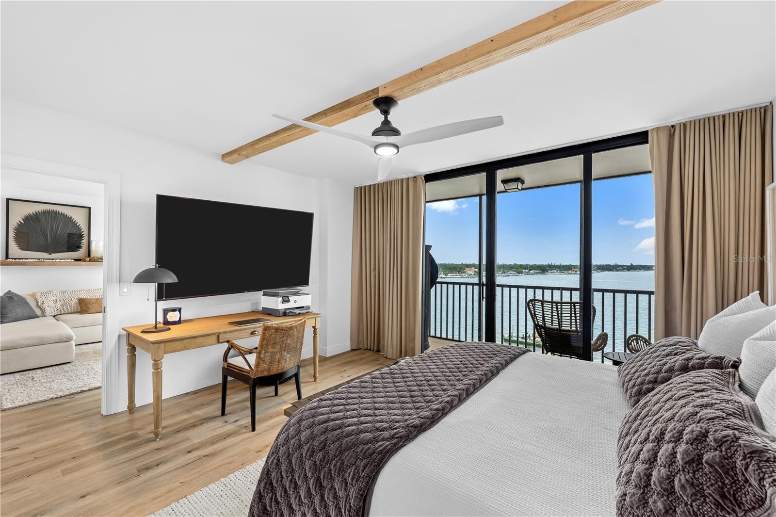 Second bedroom configured as a guest room and home-office setup with a private balcony, bay view, and motorized blinds.