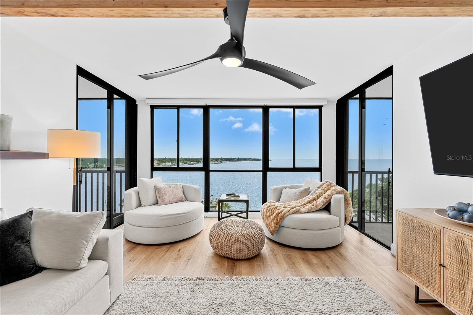 Living room with dual sliding-door balcony access, oversized swivel chairs, and wide open-water views.