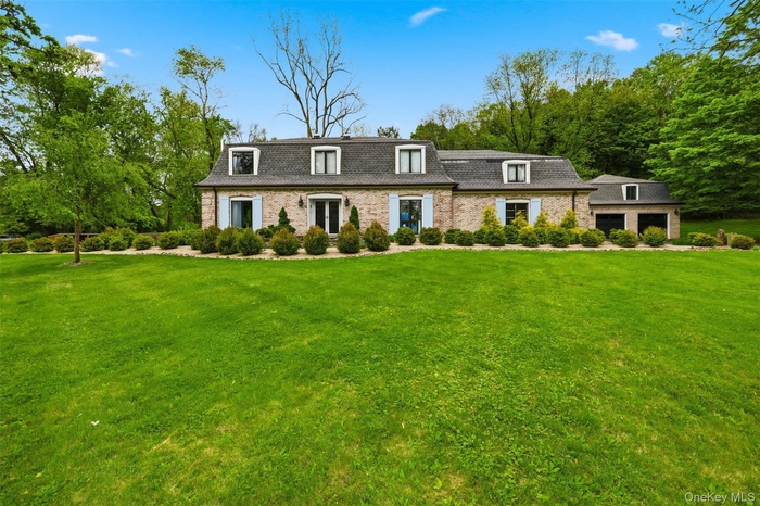 View of front of property, a detached garage, brick siding, and a gambrel roof.