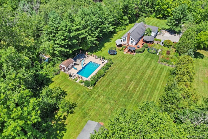 Expansive property featuring a large in-ground swimming pool with surrounding patio, a dedicated pool house, and a sizable lawn area