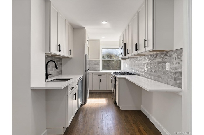 Galley kitchen featuring white shaker cabinetry, light-toned countertops, and wood-finish flooring