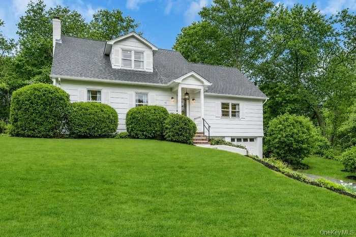 White siding exterior with a dark shingle roof, dormer window, and an attached garage