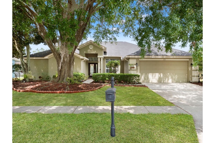 Welcoming front elevation featuring a spacious two-car garage, mature landscaping, and a well-maintained driveway with ample parking.