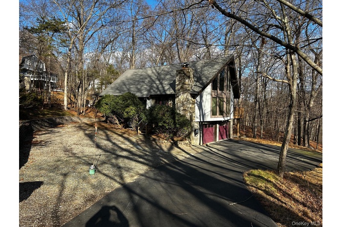 View of side of property with a chimney, driveway, a shingled roof, and a garage