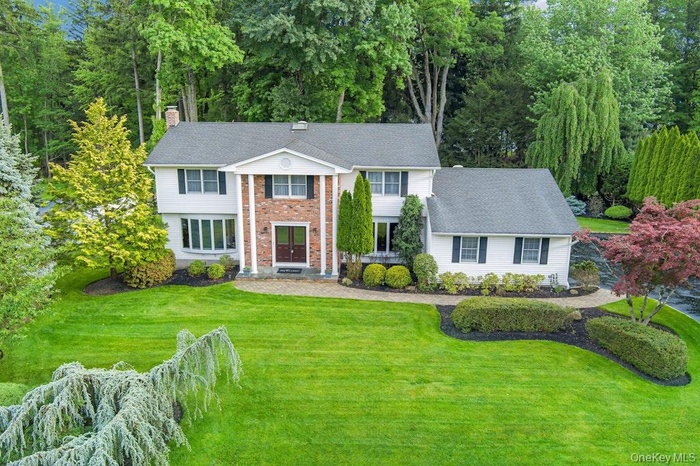 Traditional colonial home featuring a white exterior, brick accents, and beautifully manicured lawn