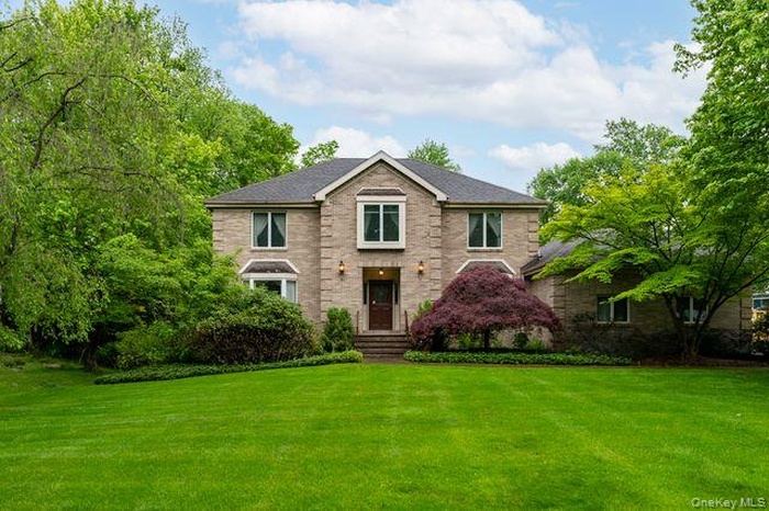 Traditional brick facade home featuring a prominent front entrance with stone steps, a manicured lawn, and mature trees