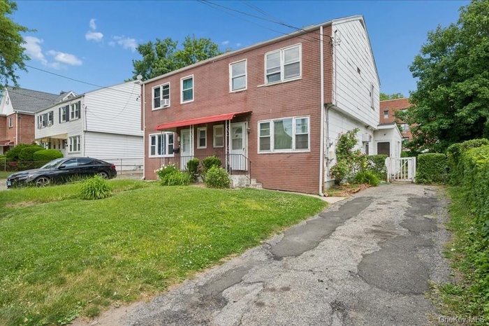 Brick and siding exterior featuring multiple windows and a front lawn