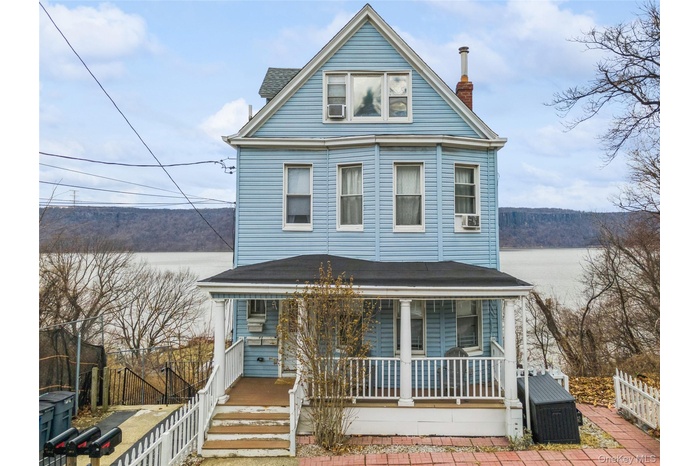 View of front of home featuring fence, a water view, a porch, a shingled roof, and a chimney
