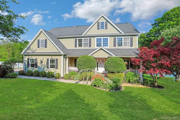 Stunning front porch colonial showcasing exceptional curb appeal, with a lush manicured lawn, mature specimen plantings, and a charming facade.