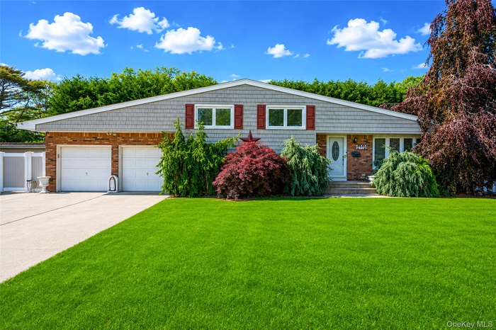 Front exterior featuring a brick and shingle facade, two-car garage, mature landscaping, and an expansive lawn