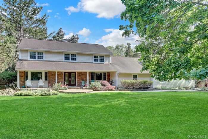 Expansive green lawn fronts a two-story residence featuring light-colored siding and a covered front porch with stone facade accents