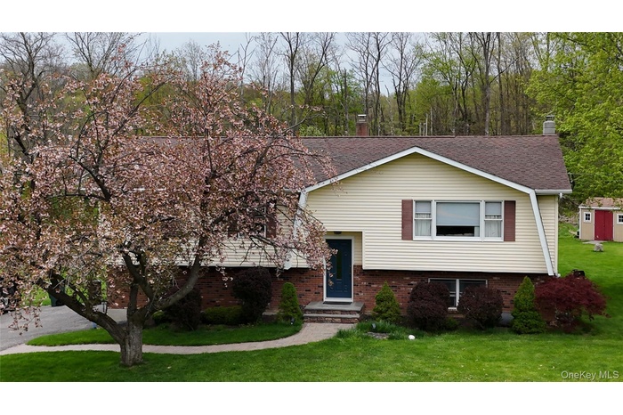 Split-level residence featuring a brick and siding exterior The front elevation features a gambrel style slice view roof line, a prominent flowering t