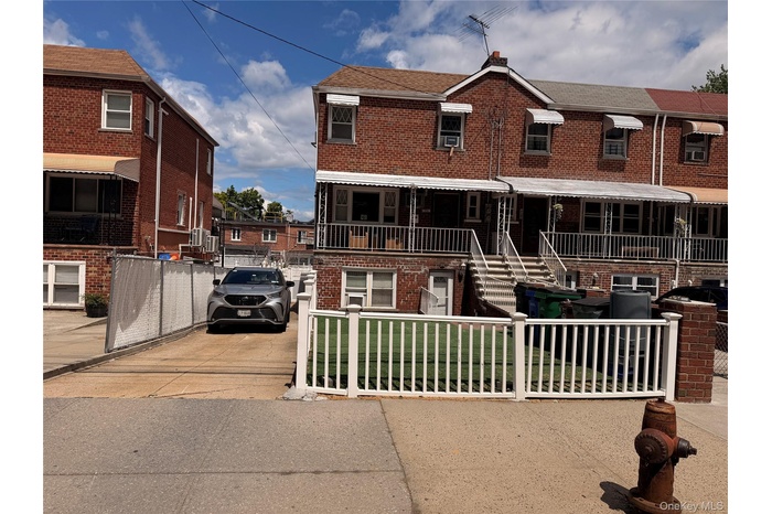 Brick facade residential property featuring a ground-level driveway, a white picket fence, an exterior staircase leading to a covered porch, and awnin