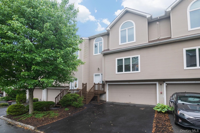 Townhome exterior featuring tan siding, a prominent arched window, and an integrated garage