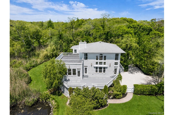 Contemporary residence with a multi-level exterior, featuring multiple balconies, a gravel driveway, mature perimeter landscaping, and a manicured law