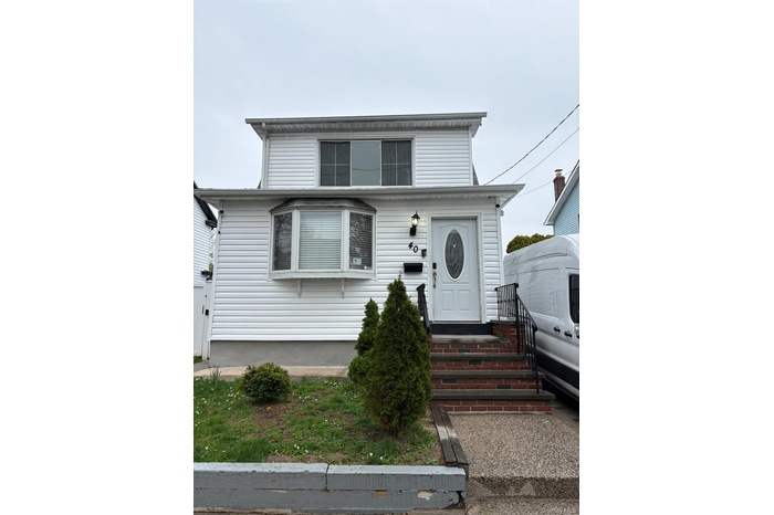White siding exterior with a bay window, a multi-pane front door, and brick-clad entry stairs