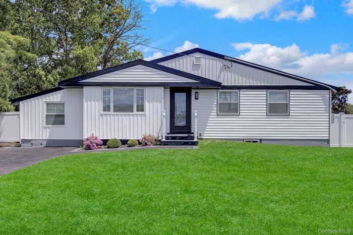 Single-story residence featuring a dark roofline contrasting with white siding, a landscaped front garden with plantings, a paved driveway, and a vibr