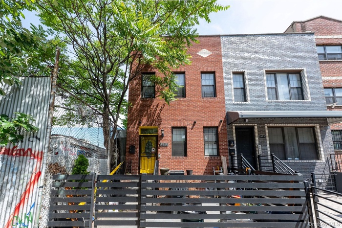 Brick facade townhome featuring a vibrant yellow entry door, black security bars on windows, and a multi-level black fence