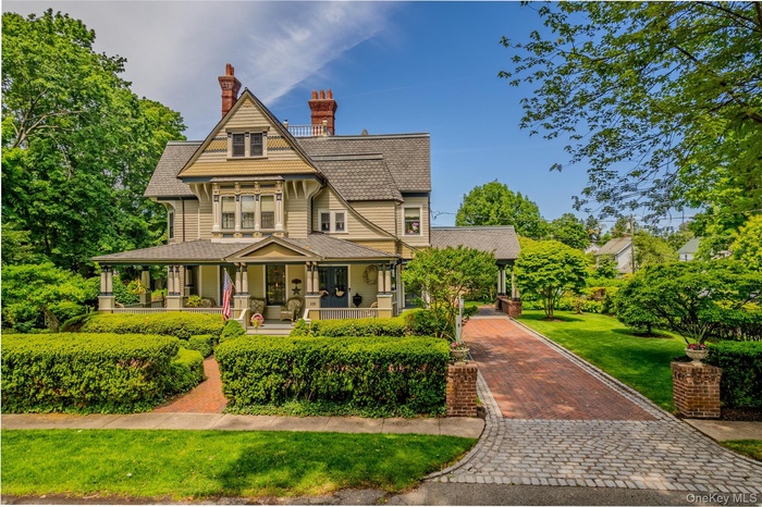 Victorian-style residence featuring a prominent front porch with columns, a multi-gabled roofline, and brick chimneys