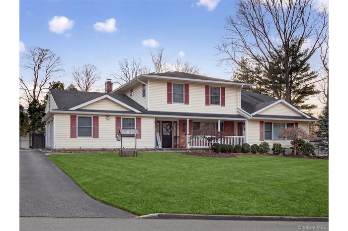 Traditional-style house featuring a porch, a chimney, a front lawn, and a shingled roof