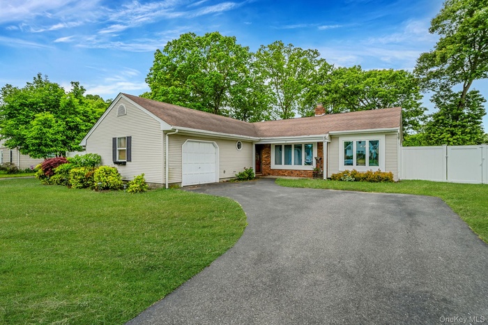 Ranch-style exterior with vinyl siding, an attached garage, a paved driveway, mature landscaping, and white privacy fence