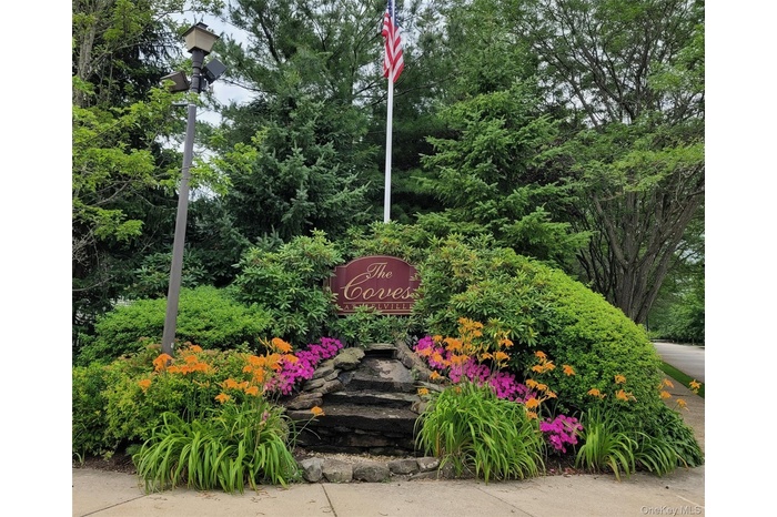 Gated Entry featuring a decorative sign, tiered stone landscaping, and vibrant floral plantings