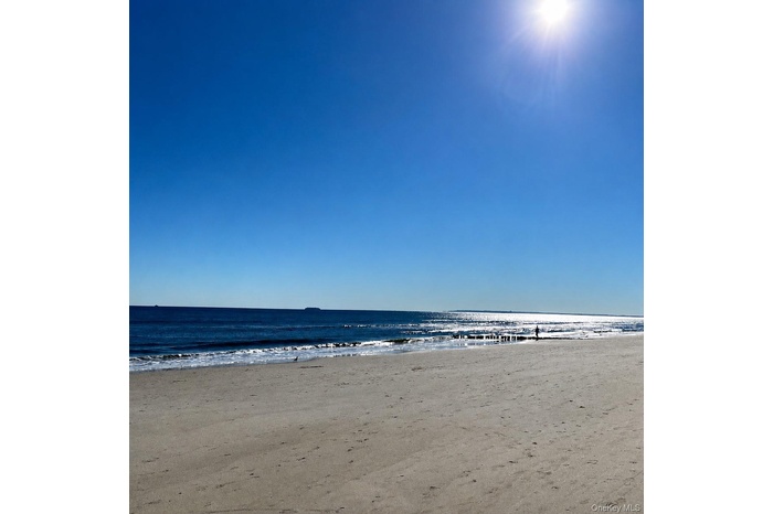 Expansive sandy beach with ocean waves, bright blue sky, and distant horizon