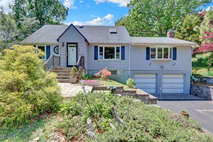 Split-level residence featuring a light gray exterior with dark blue shutters and a prominent front entry with decorative side panels