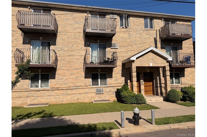 Brick exterior building featuring multiple private balconies with decorative metal railings, a covered entrance with a gabled roofline, and ground-lev