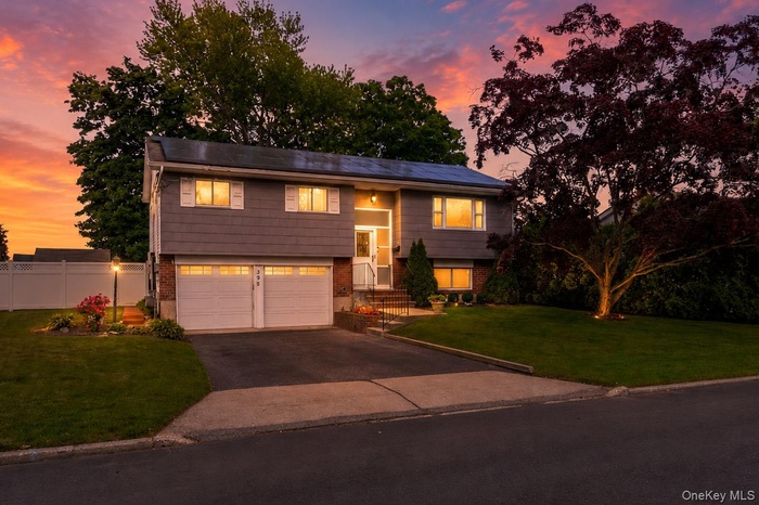 Split-level residence featuring gray siding, a two-car garage with white doors, and a paved driveway