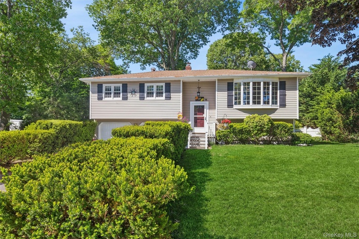 Split-level residence featuring light toned siding, a bay window with multiple panes, and a front entry with storm door
