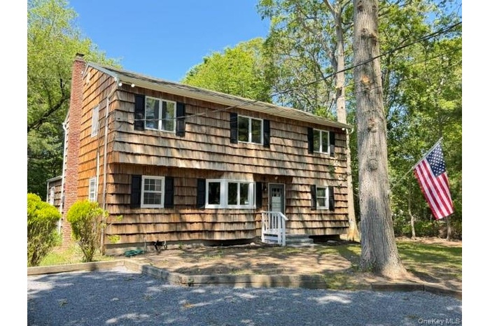 Two-story cedar shake exterior featuring black shutters, white window trim, and a prominent brick chimney