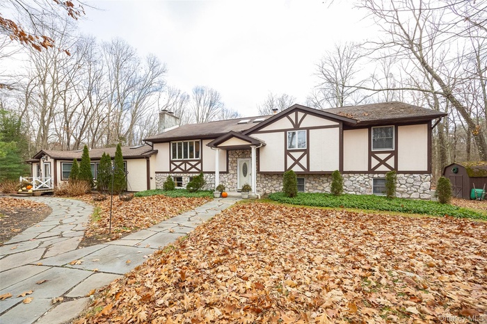 View of front of house with stucco siding, a chimney, and stone siding