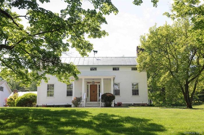 White siding exterior featuring a covered porch with white columns, a natural wood front door, and a metal roof