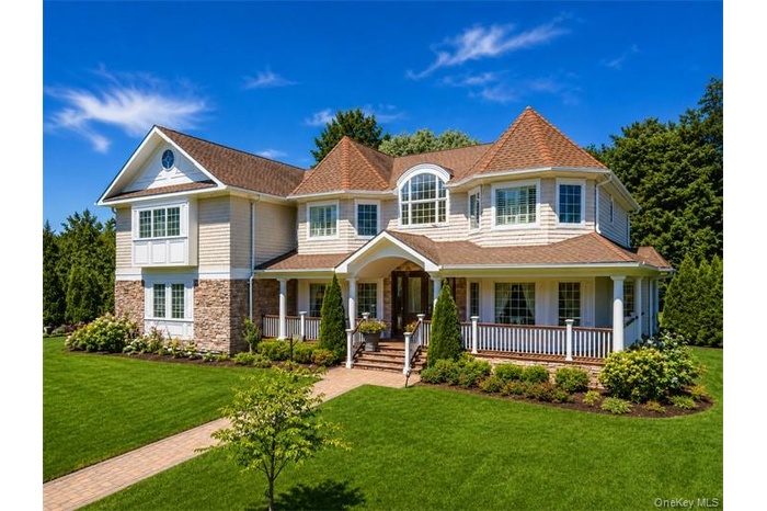 Expansive lawn with a brick paver pathway leading to a two-story residence featuring a covered porch, stone accents, and shake siding