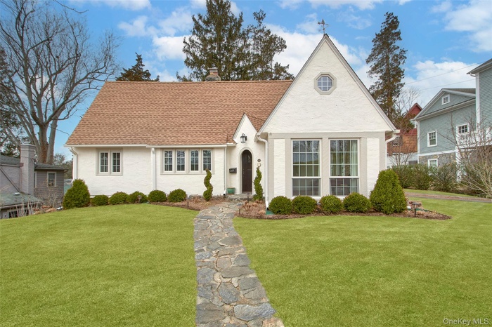 View of front facade with a chimney, a shingled roof, and a front lawn