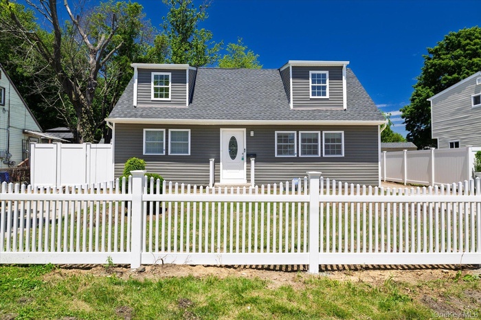 Gray siding residence featuring a white picket fence, a white oval-lite entry door, and two dormer windows
