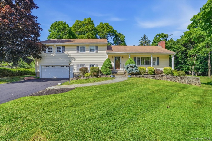 Split-level residence featuring a two-car garage, established front yard landscaping, stone retaining wall, covered front porch with columns, and a pa