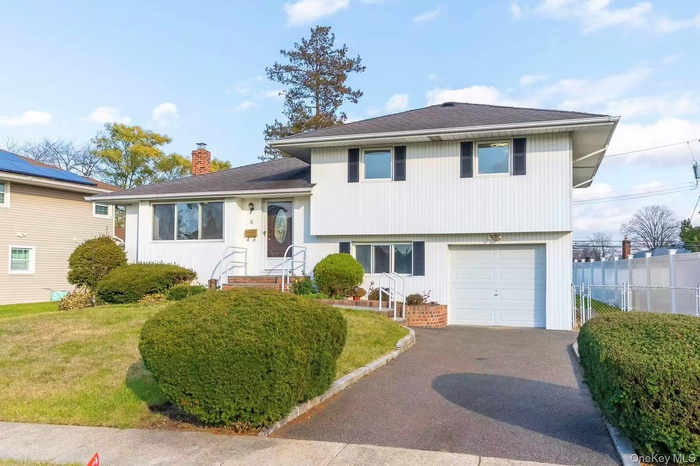 Tri-level home featuring a chimney, driveway, an attached garage, and roof with shingles