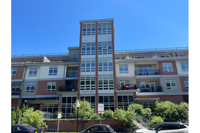 Multi-story residential building featuring a brick and siding exterior, expansive window panels, private balconies with black railings, and a prominen