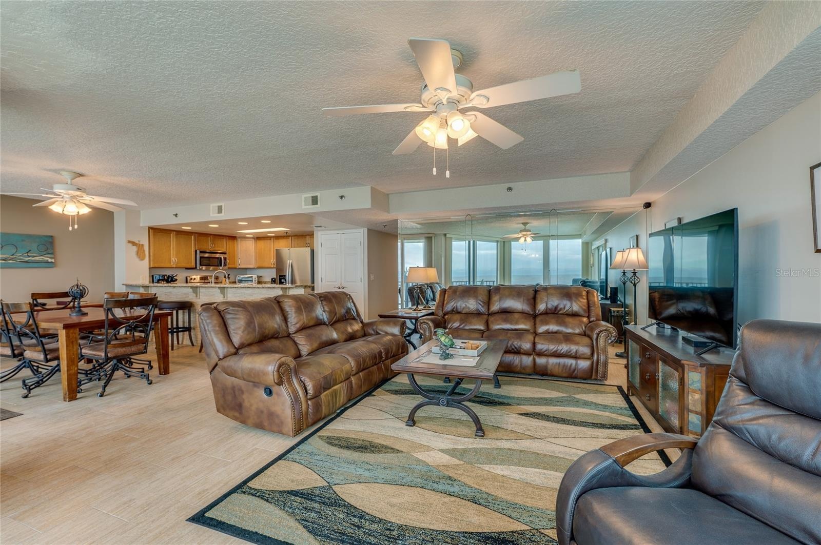 The spacious open-concept design combines living, dining, and kitchen areas, offering coastal views, recessed lighting, and a mirrored accent wall tha